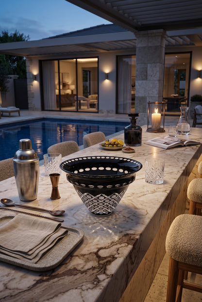 Noctura Crest Bowl on an outdoor marble table beside glassware and a swimming pool