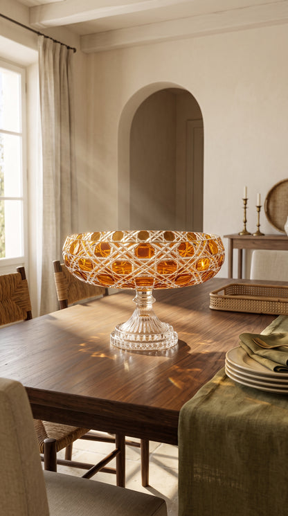 Verdura Sunlit Amber pedestal bowl on a sunlit dining table beside stacked plates