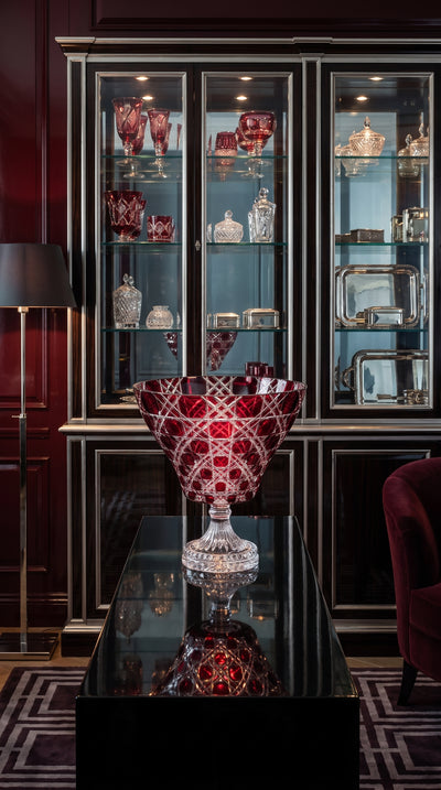Crimson Red Verdura Trumpet Bowl before a glass cabinet in a burgundy paneled room.
