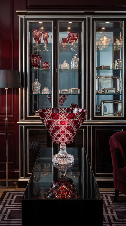 Crimson Red Verdura Trumpet Bowl before a glass cabinet in a burgundy paneled room.