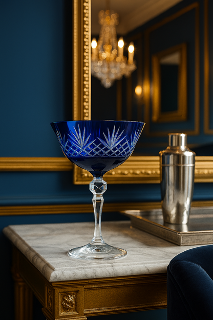 Midnight Sapphire Veyra Coupe on a marble side table beside a cocktail shaker in a blue salon.