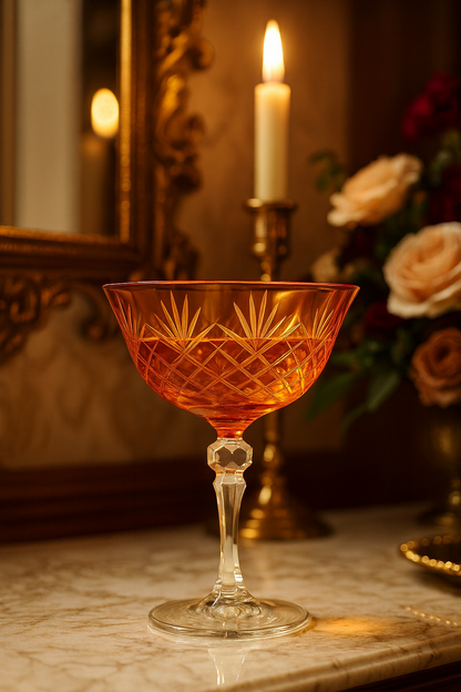 Sunlit Amber Veyra coupe glass on marble beside a candle and flowers